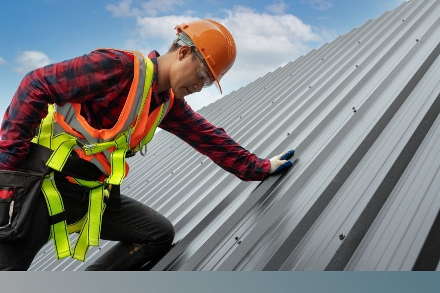 roofer in personal protective equipment screws down metal roof panels